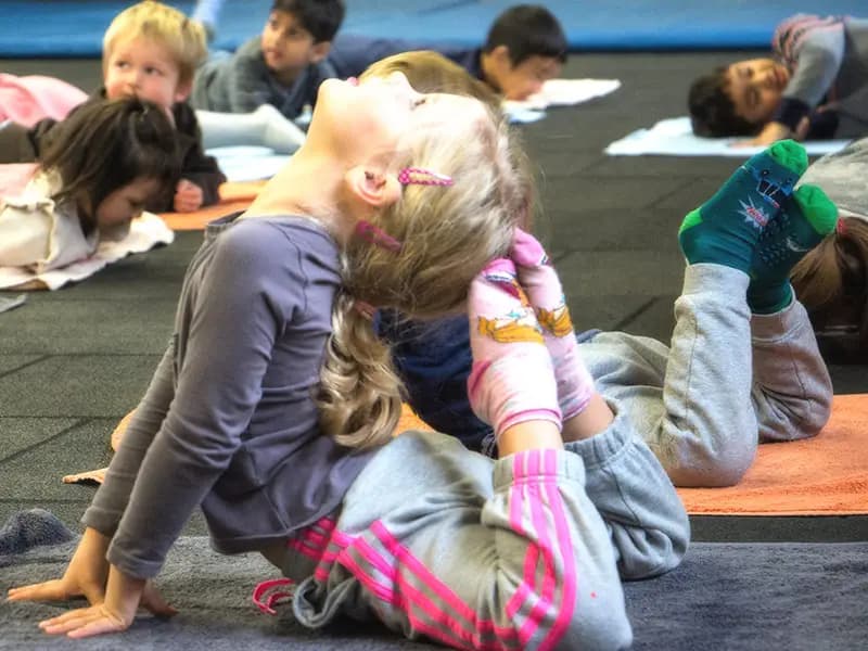 Children practicing yoga stretches on mats in the TIMS gym