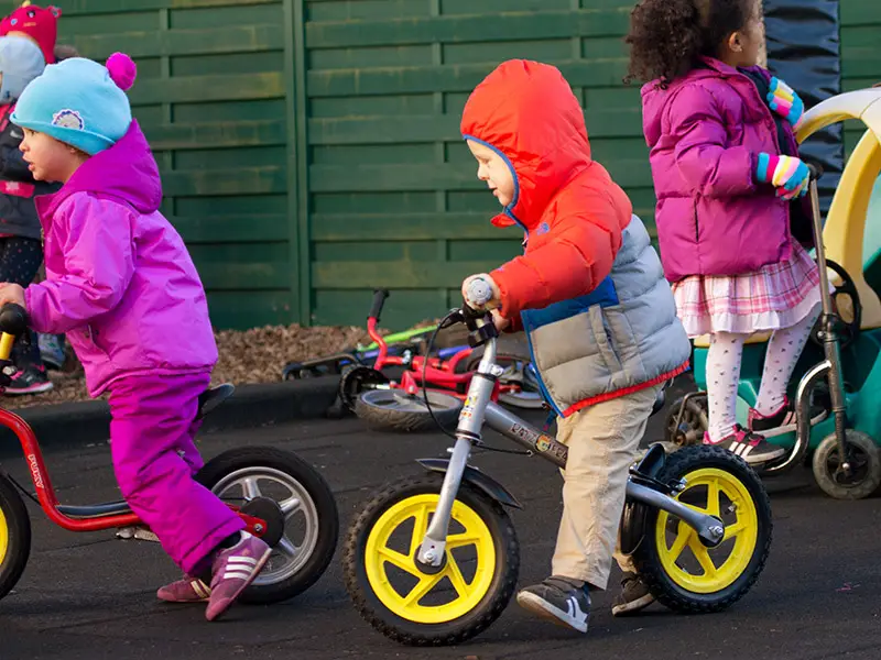 Three toddlers riding balance bikes together in the outdoor play area