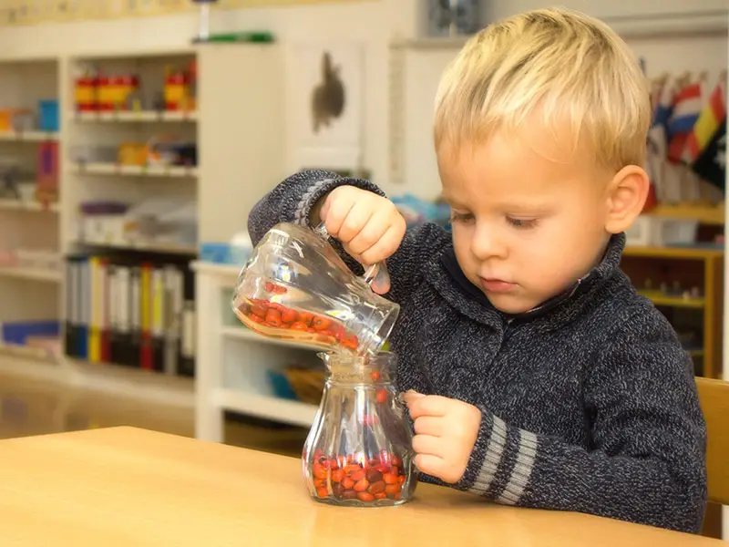 Young boy practicing a Montessori pouring exercise with glass jars