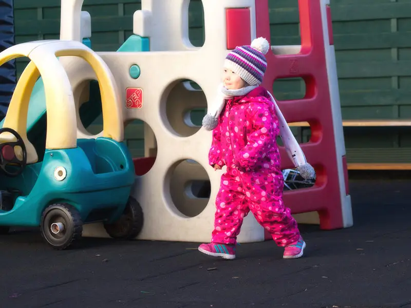 Toddler girl in a pink snowsuit walking near the playground climbing structure