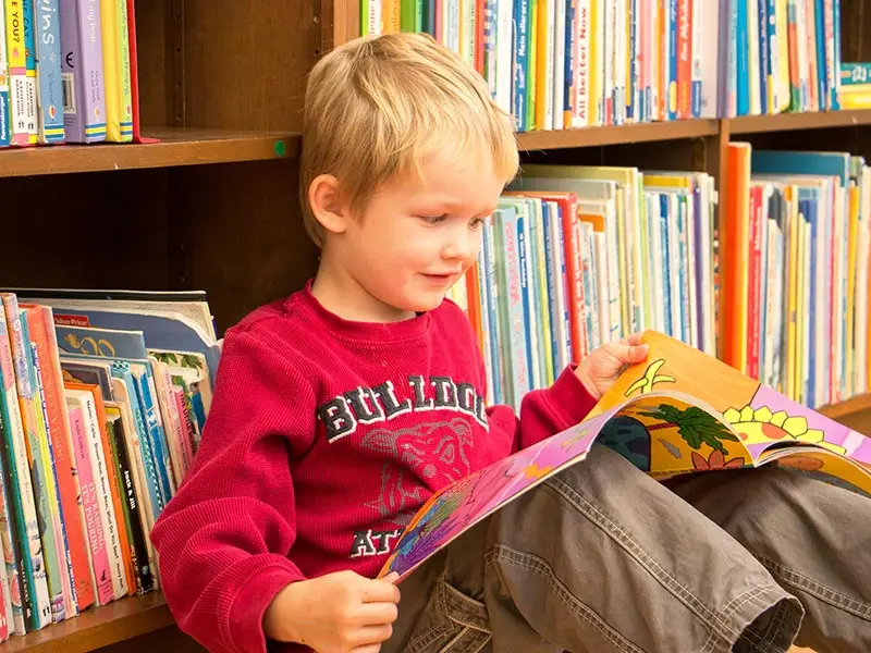 Boy reading a picture book in front of a classroom bookshelf