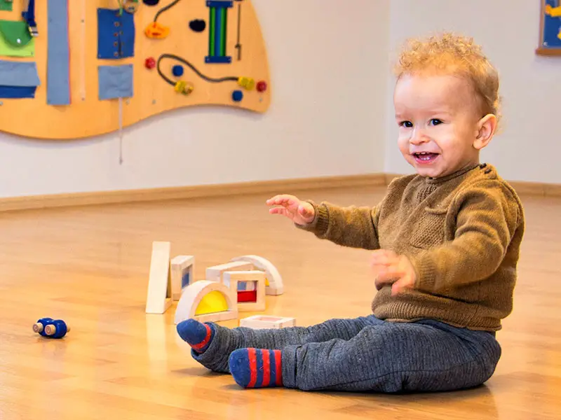 Toddler in the ages 1-3 classroom choosing a practical life tray from the shelf
